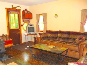 A living room with a sofa, a television, a wooden cabinet, and a door. - Cozy Vacation Cabin near Allegheny State Forest, Pennsylvania (Penfield)