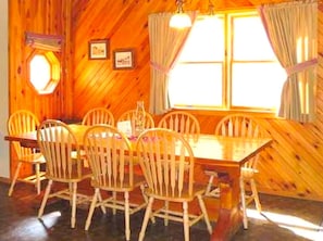 Un comedor de madera con una mesa y sillas, una ventana con cortinas y una lámpara fijada a la pared.