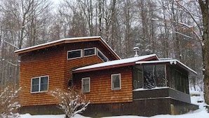 A wooden cabin with a sloped roof, a large window, and a chimney. - Cozy Vacation Cabin near Allegheny State Forest, Pennsylvania (Penfield)