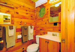 A wooden cabin bathroom with a toilet, sink, and towel rack.