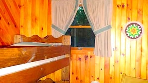 A wooden cabin interior with a bunk bed, a window with curtains, a lamp, and a wall decoration. - Cozy Vacation Cabin near Allegheny State Forest, Pennsylvania (Penfield)