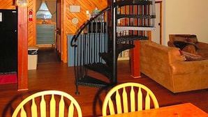 A wooden interior with a spiral staircase, a dining area with chairs, and a living room with a sofa. - Cozy Vacation Cabin near Allegheny State Forest, Pennsylvania (Penfield)