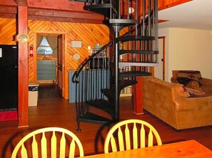 A wooden interior with a spiral staircase, a dining area with chairs, and a living room with a sofa. - Cozy Vacation Cabin near Allegheny State Forest, Pennsylvania (Penfield)
