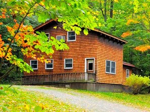 A wooden cabin with a porch, surrounded by autumn foliage.