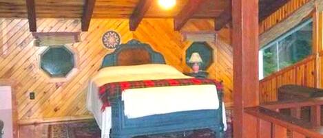 Un dormitorio de cabaña de madera con una cama, un tapete y una ventana.