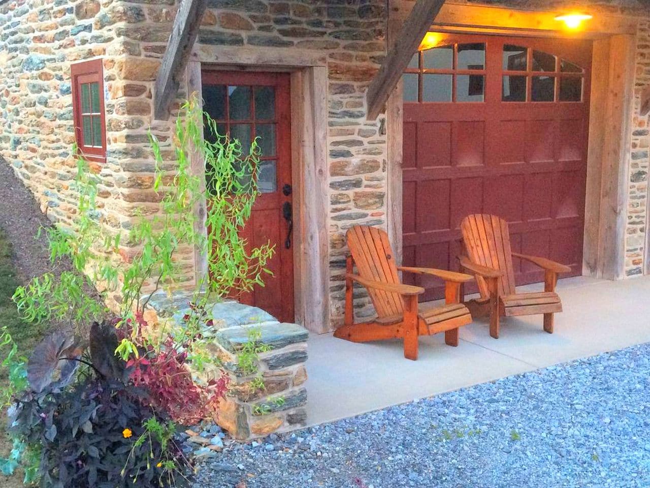 A stone building with a red door, two wooden chairs outside, and a gravel path.