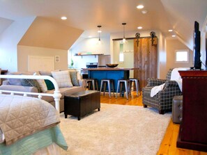 A spacious loft with a high ceiling, a kitchen area, and a living room with a sofa and ottoman. - Stylish Cottage Loft Rental on a Farm in Lancaster County near Philadelphia, Pennsylvania (Christiana)