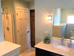 A bathroom with a white door, a shower, a glass jar on the sink, and a mirror above the sink. - Stylish Cottage Loft Rental on a Farm in Lancaster County near Philadelphia, Pennsylvania (Christiana)