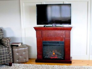 Ein Kamin mit Fernseher darauf, ein Karosobaru und ein gepolsterter Hocker.