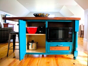 Une cuisine équipée d’un four à micro-ondes, avec un saladier rouge et une casserole posée sur le plan de travail.