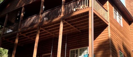 Une cabane en bois dotée d’un balcon, de nombreuses fenêtres et d’une cour gazonnée.