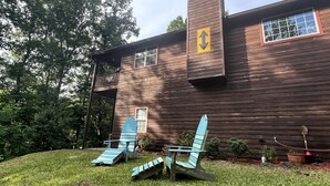 A wooden cabin with a chimney, a porch with Adirondack chairs, and a small garden area. - Spacious Camping Cabin Perfect for Families in the Blue Ridge Mountains of Georgia (Blairsville)