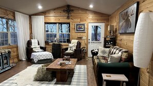 A cozy log cabin interior with a wooden floor, a checkered rug, a wooden coffee table, a sofa, a chair, and a fireplace. - Spacious Camping Cabin Perfect for Families in the Blue Ridge Mountains of Georgia (Blairsville)