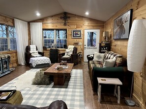 A cozy log cabin interior with a wooden floor, a checkered rug, a wooden coffee table, a sofa, a chair, and a fireplace. - Spacious Camping Cabin Perfect for Families in the Blue Ridge Mountains of Georgia (Blairsville)