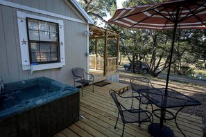 A deck with a hot tub, outdoor chairs, and a table with an umbrella. - Rustic Dog-Friendly Cabin with Private Deck and Hot-Tub in Texas (Wimberley)