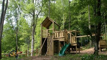 Une structure de jeux en bois située dans une zone boisée, avec un toboggan.