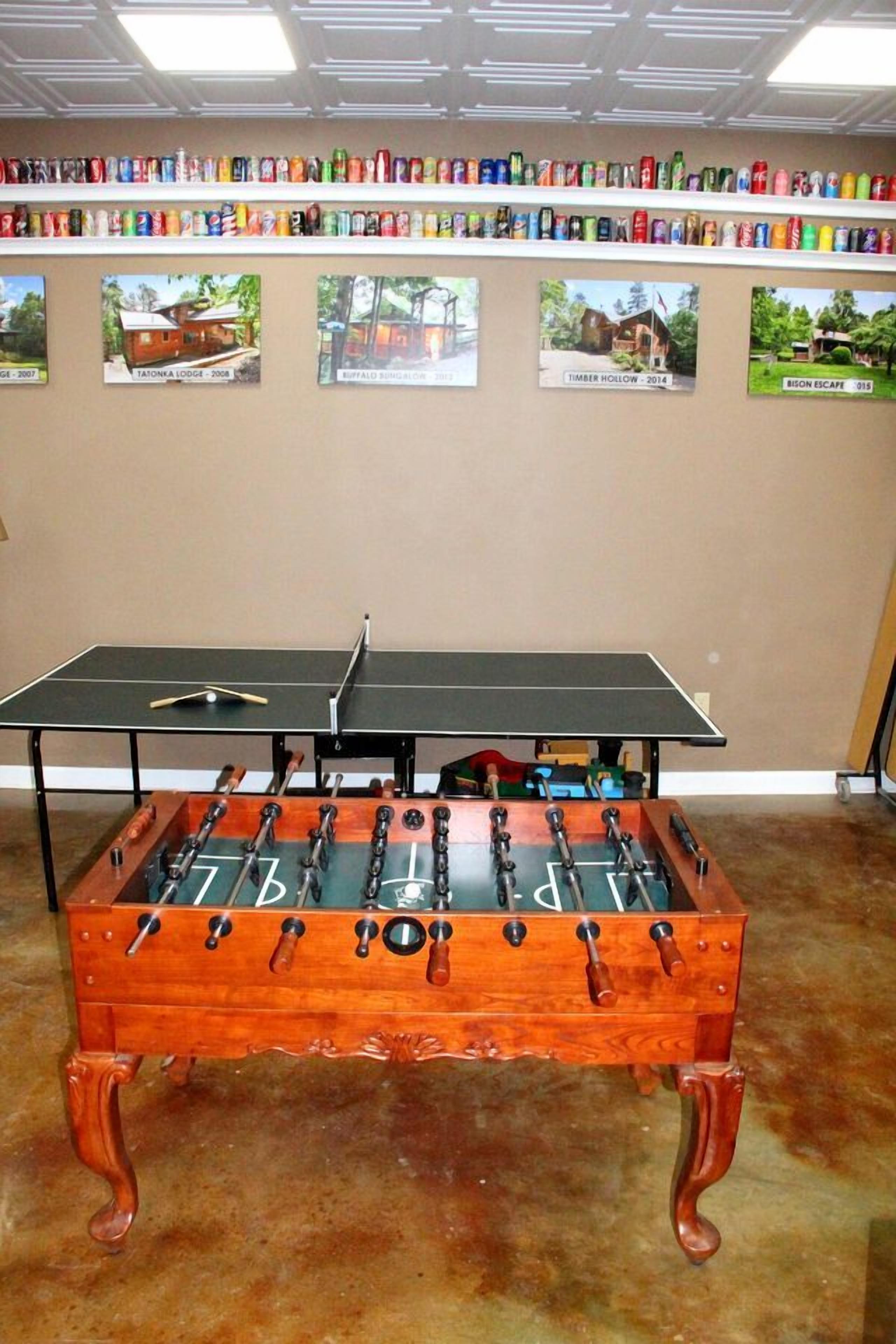 A foosball table with a ping pong table in front, surrounded by shelves of soda cans.