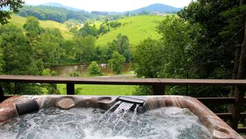 A hot tub with a wooden deck overlooking a green landscape and a body of water.