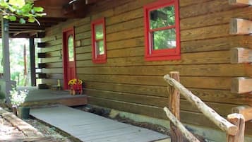 Una rustica baita di tronchi con un portico in legno, una porta rossa e una piccola scala che conduce all'ingresso.
