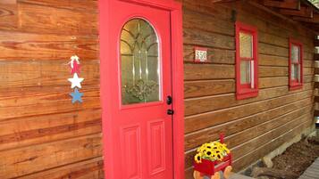 A wooden cabin with a red door, a mailbox, and a number sign.
