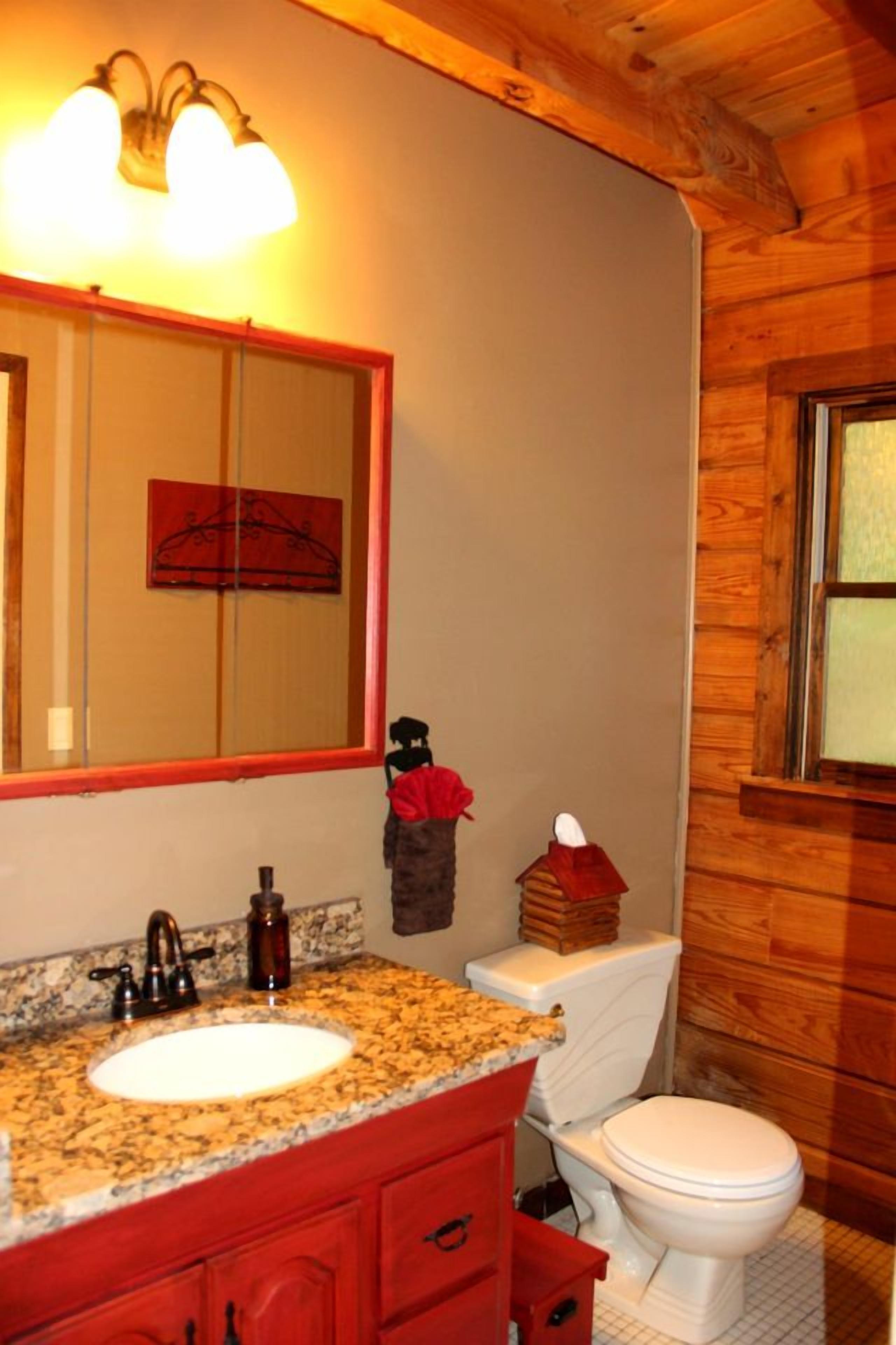 A bathroom with a granite countertop sink, a mirror with a red frame, a white toilet, and a wooden wall.