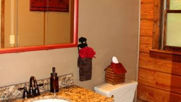 A bathroom with a granite countertop sink, a mirror with a red frame, a white toilet, and a wooden wall.