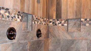 A shower with wooden paneling and stone tiles, including a pebble-patterned floor.