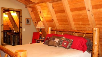 Una stanza con soffitto spiovente, travi in legno, un letto con biancheria rossa, una lampada e una poltrona rossa.