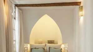 A bedroom with a large bed, a bedside table, a decorative bench, and a unique arched ceiling.
