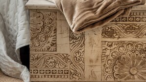A bed with a quilted cover, a decorative headboard, and a bedside table with a towel.