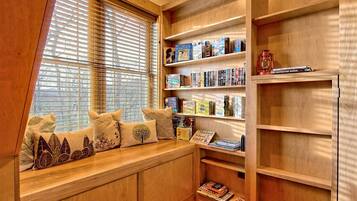 A cozy reading nook with a built-in bench, wooden shelves, and a window with blinds.