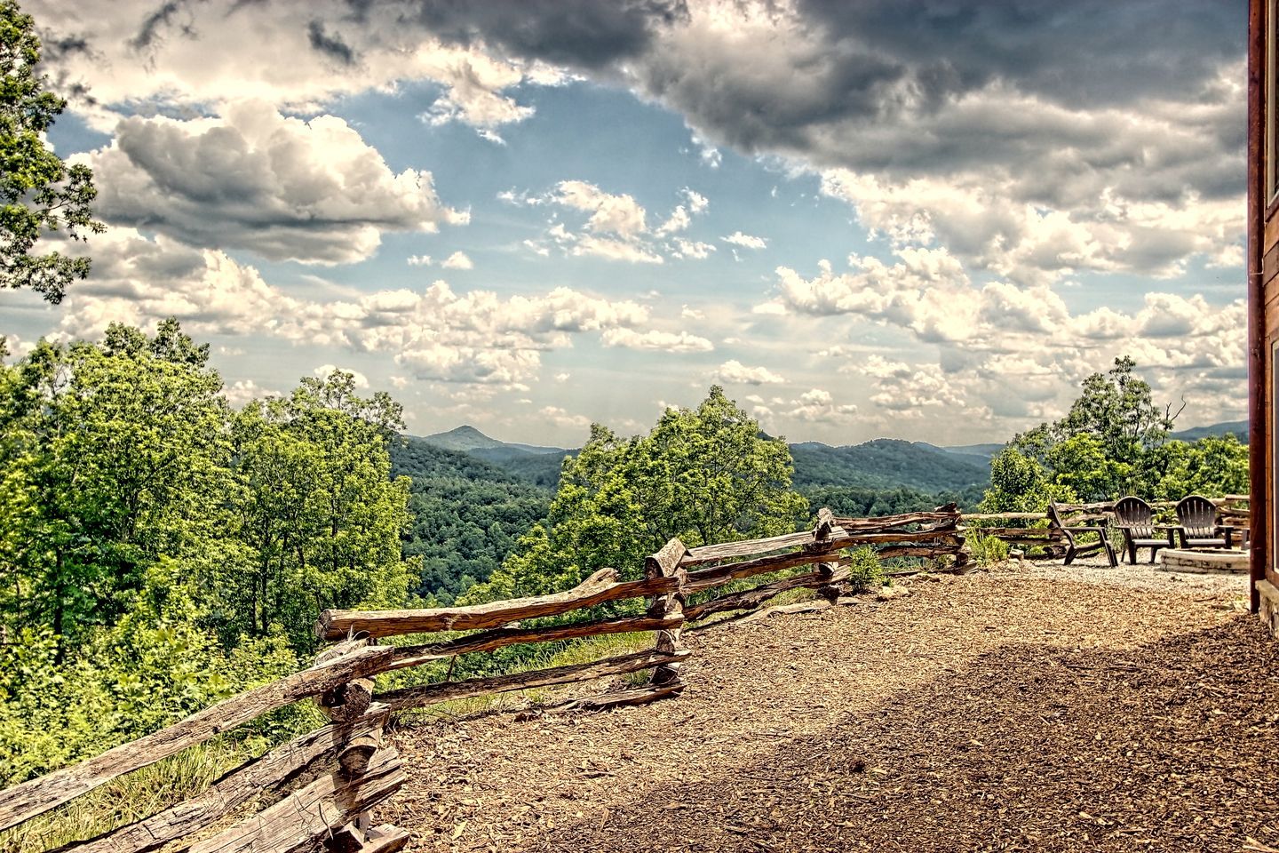 A rustic wooden fence, a gravel path, and a view of a forested mountain range.
