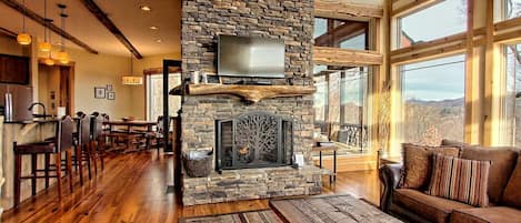 A spacious living area with a stone fireplace, wooden furniture, and large windows offering a view.