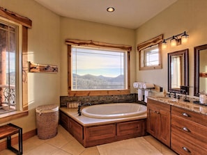 A bathroom with a large bathtub, wooden cabinetry, a window with a mountain view, and a sink with a vanity.