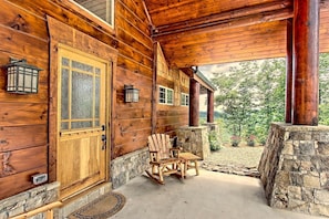 A wooden cabin with a stone porch, a wooden door, and two rocking chairs.