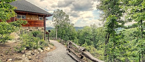 En rustik hytte med en grusvej, der fører hen til den, omgivet af tæt skov og en klar himmel.