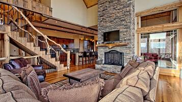 A spacious living area with a stone fireplace, a wooden staircase, and a large window overlooking a scenic view.