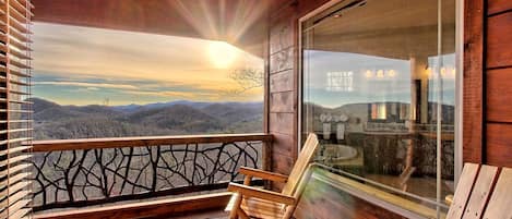 A wooden deck with two chairs and a glass wall overlooking a mountainous landscape.