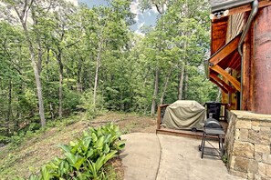 A wooden cabin with a stone foundation, a covered grill, and a concrete pathway leading to the entrance.