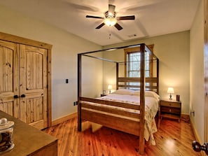 A four-poster bed with a wooden frame, a ceiling fan, and a nightstand with a lamp.