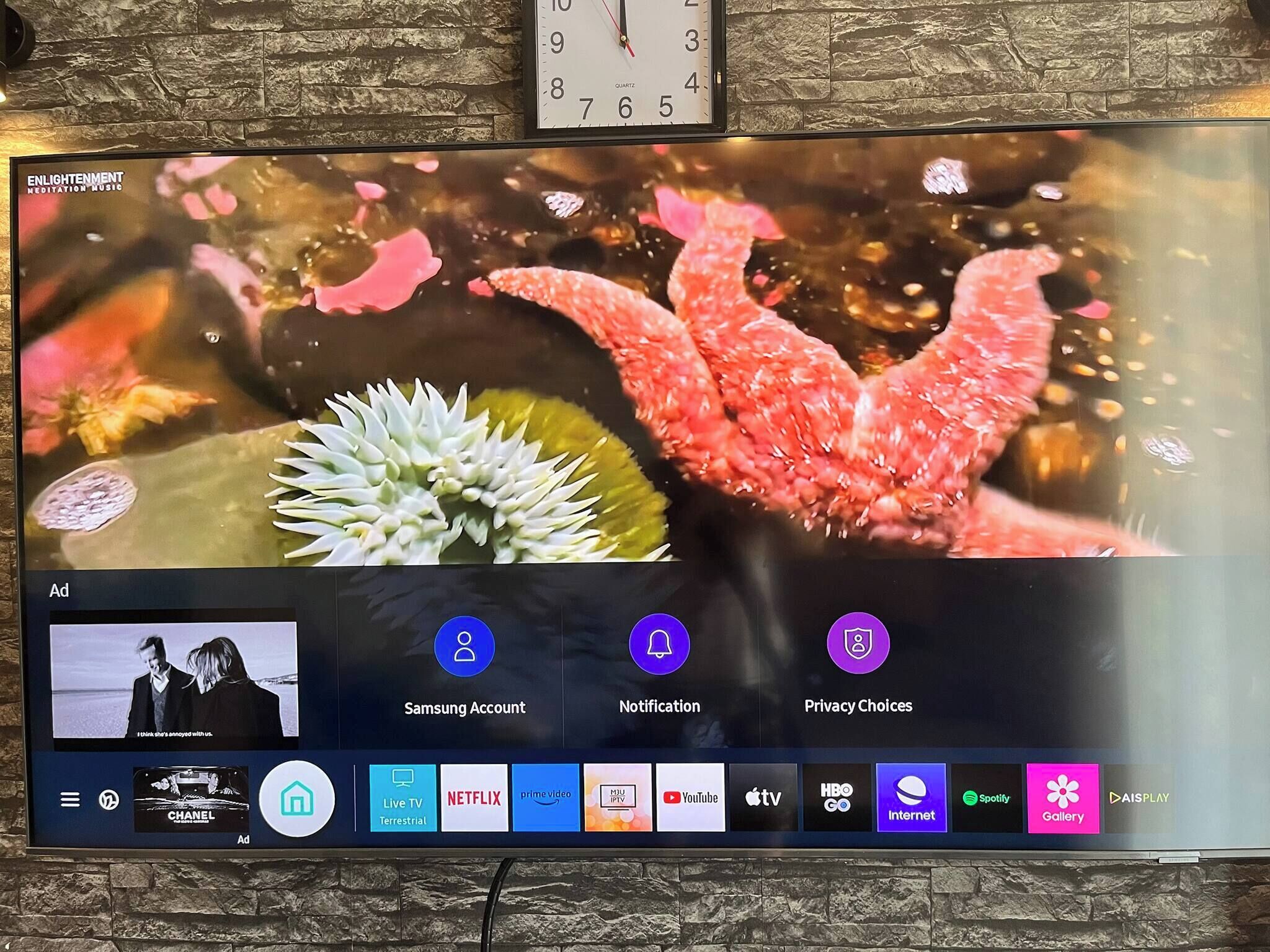 Et fjernsyn der viser en reklame for meditationsmusik, med ikoner for Samsung Konto, Notifikationer og Privatlivsindstillinger, samt en menulinje med forskellige streamingtjenester.