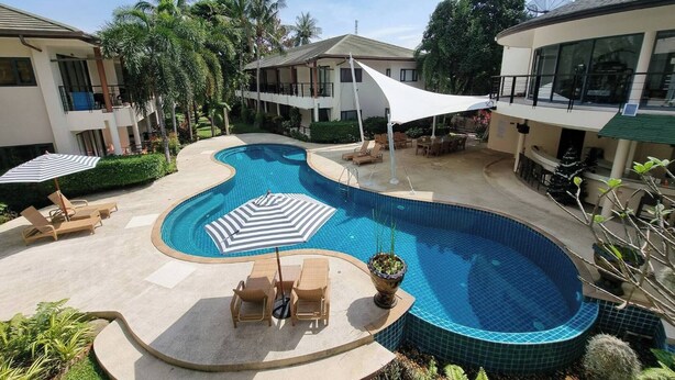 A swimming pool with lounge chairs and umbrellas, surrounded by greenery and buildings. - Apartment Eliza Samui in Garden Resort With Shared Pool (Koh Samui)