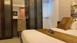 A bedroom with a bed, a wardrobe, a mirror, and a brick wall. - Apartment Eliza Samui in Garden Resort With Shared Pool (Koh Samui)