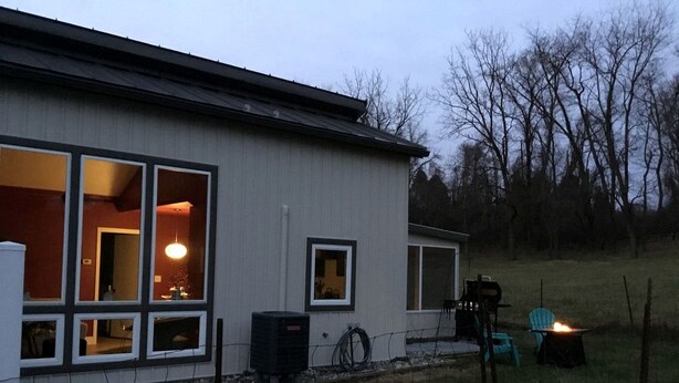 A single-story building with large windows, a visible air conditioning unit, and a fire pit in the yard. - Modern Cottage Rental on a Peaceful Farm near Amish Country in Pennsylvania (Columbia)