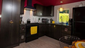 A compact kitchen with dark cabinetry, a black stove, and a window with a view of greenery. - Modern Cottage Rental on a Peaceful Farm near Amish Country in Pennsylvania (Columbia)