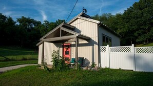 A single-story building with a covered porch, a red door, and a white fence. - Modern Cottage Rental on a Peaceful Farm near Amish Country in Pennsylvania (Columbia)