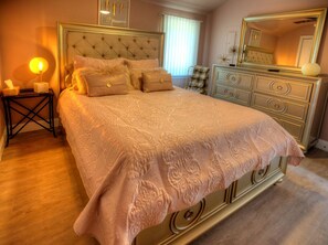 Ein Schlafzimmer mit einem großen Bett, einem Schminktisch, einem Nachttisch und einem Spiegel.
