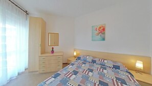 Ein Schlafzimmer mit Bett, Schminktisch, Spiegel, Nachttisch und einem Wandbild.
