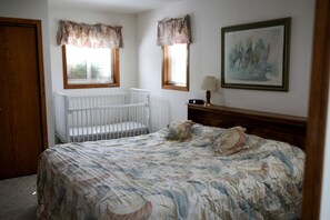 Ein Schlafzimmer mit einem Reisebett, einem Bett mit floraler Bettwäsche, einem Nachttisch, einer Lampe und einem Bild an der Wand.