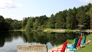 Blick auf einen See mit einem 'KEINE LEUTE RETTEN' Schild, einem Steg und bunten Adirondack-Stühlen.